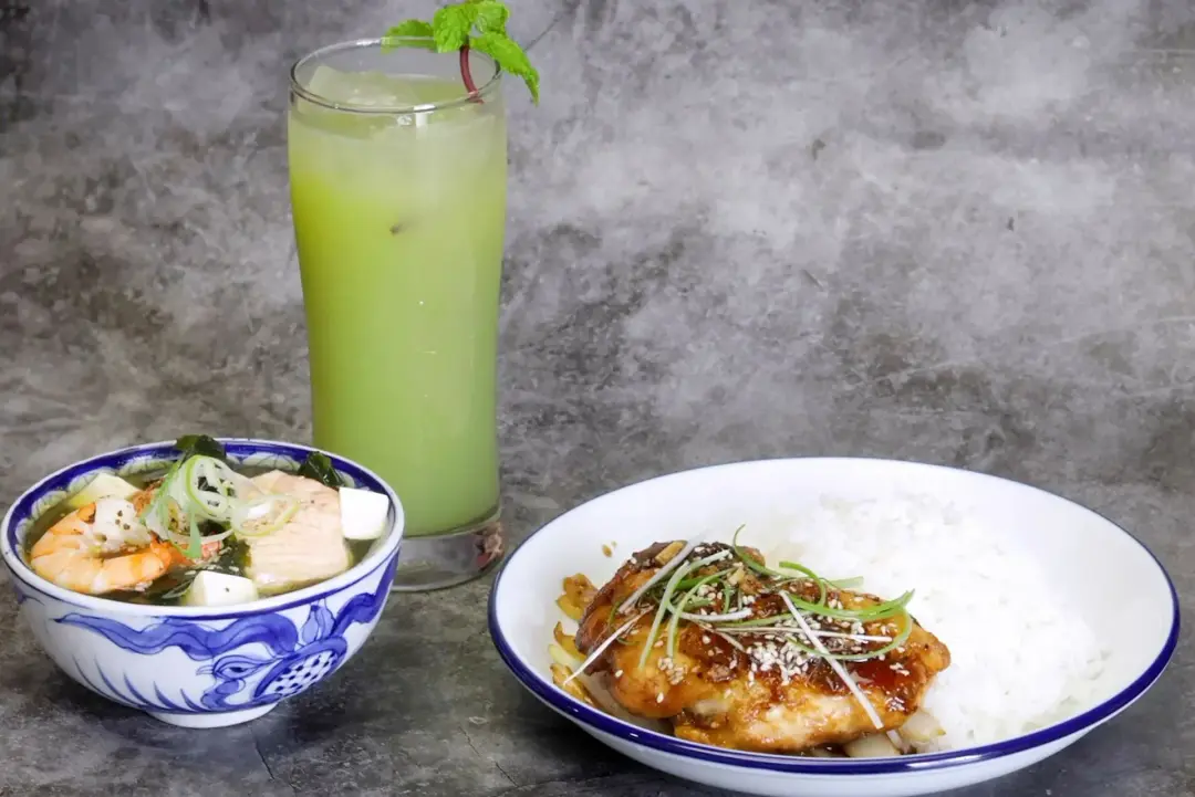 A whole meal of teriyaki chicken and rice in a plate, a small bowl of soup, and a green juice