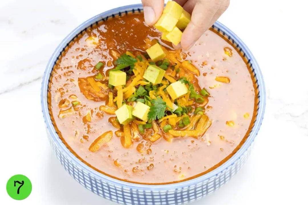 A hand putting mini squash mini cubes into a bowl of Chicken Tortilla Soup