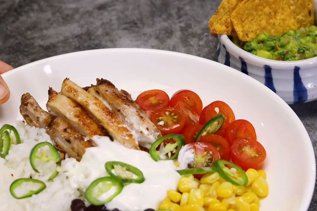 a plate of cooked chicken carnitas, half tomatoes, slices jalapeno, corn and dressing on a plate