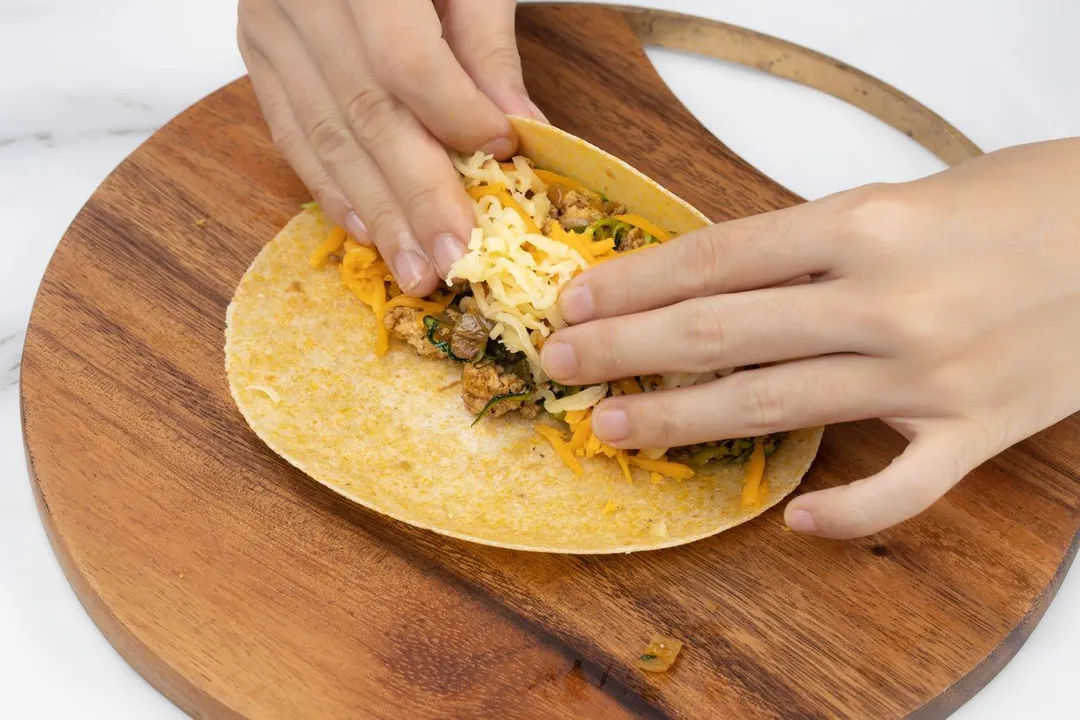hands rolling a tortilla on a cutting board