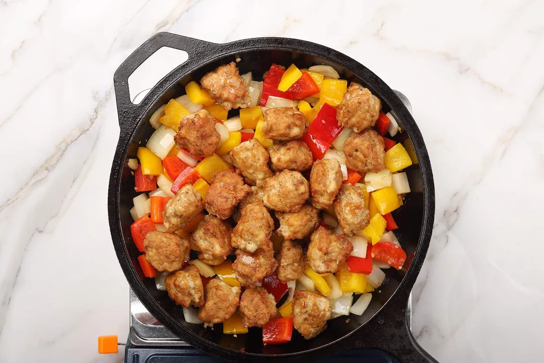 cooking chicken scoops, red and yellow diced bell pepper and diced onion in a skillet