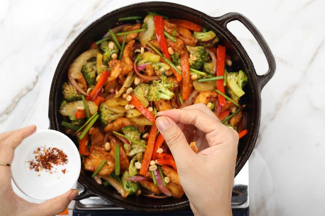 sprinkle red pepper flakes from a small bowl into a cast iron skillet of hunan chicken