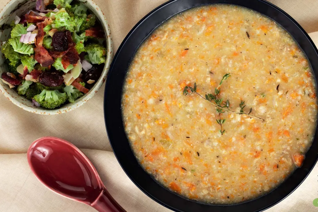 a bowl of soup next to a small bowl of salad and a ceramic spoon