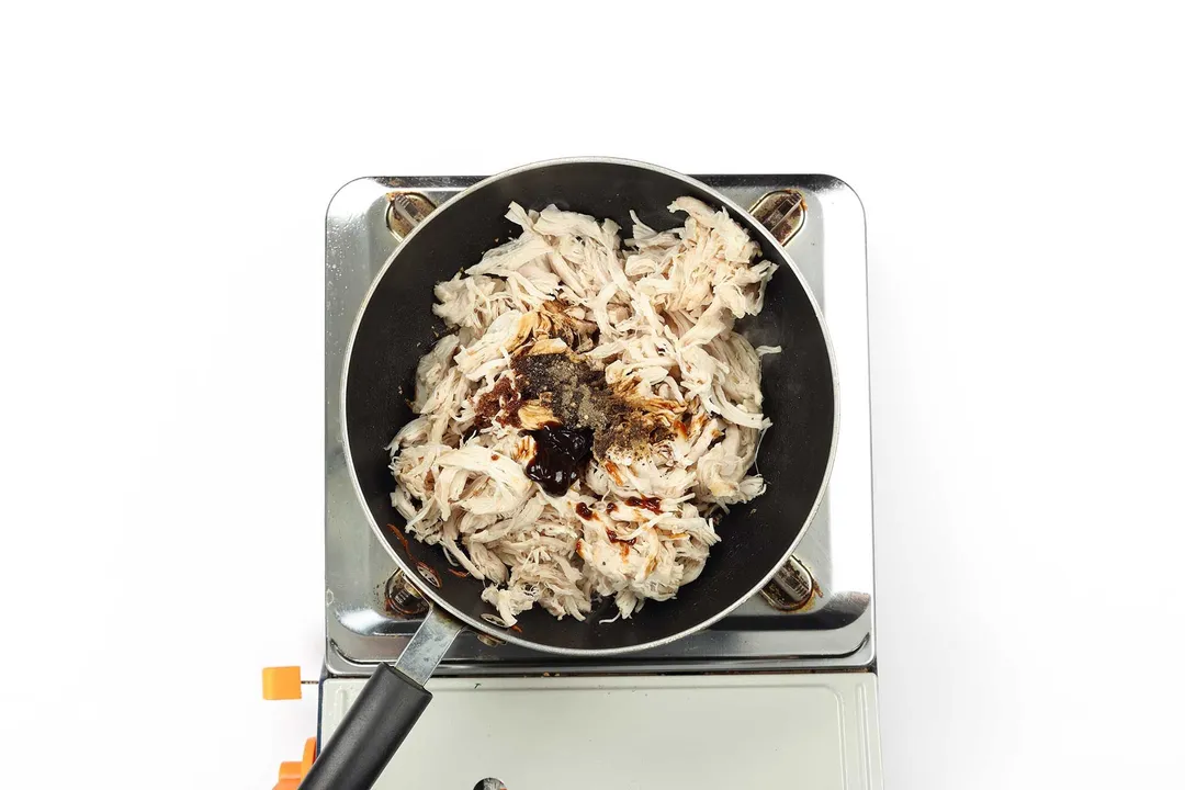 Shredded chicken breasts with seasoning in a pan