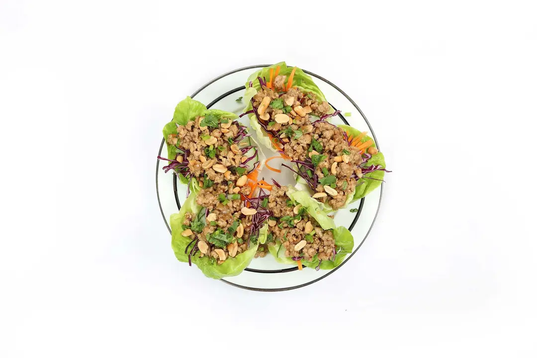 A plate containing five lettuce wraps placed on a white background