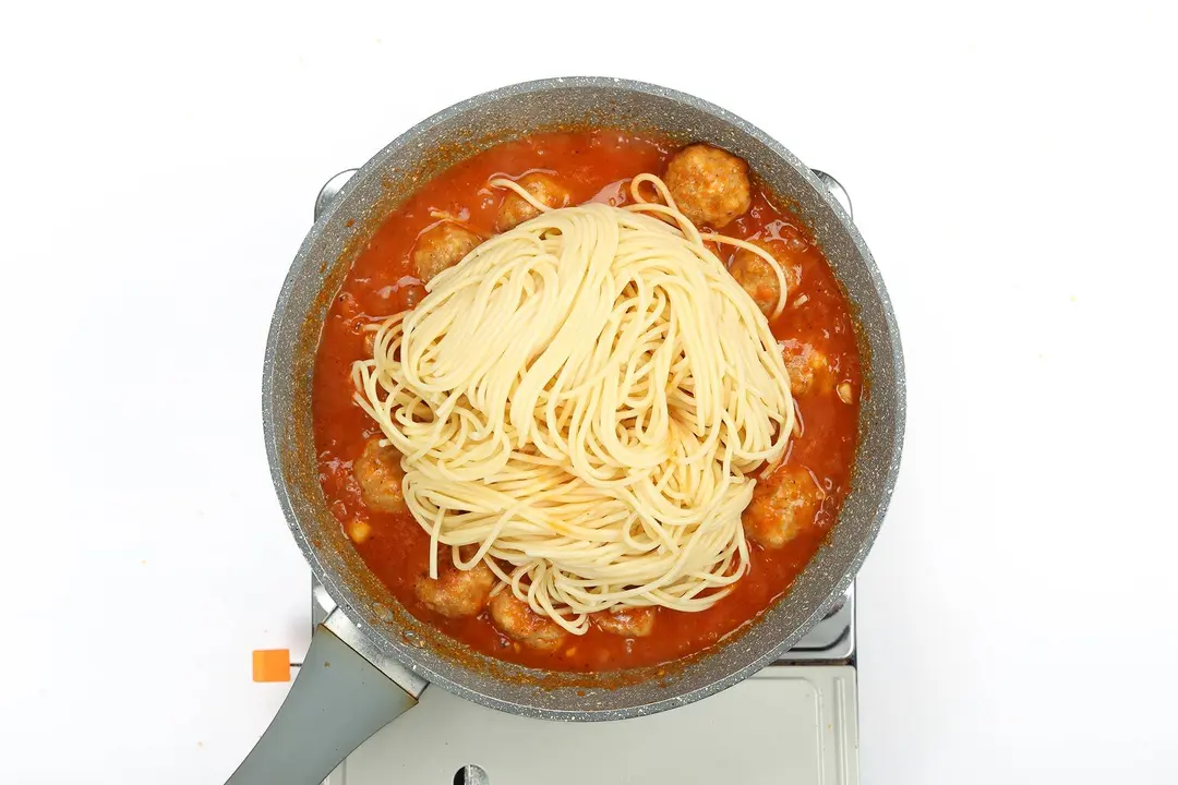 Spaghetti being cooked with chicken meatballs in tomato sauce