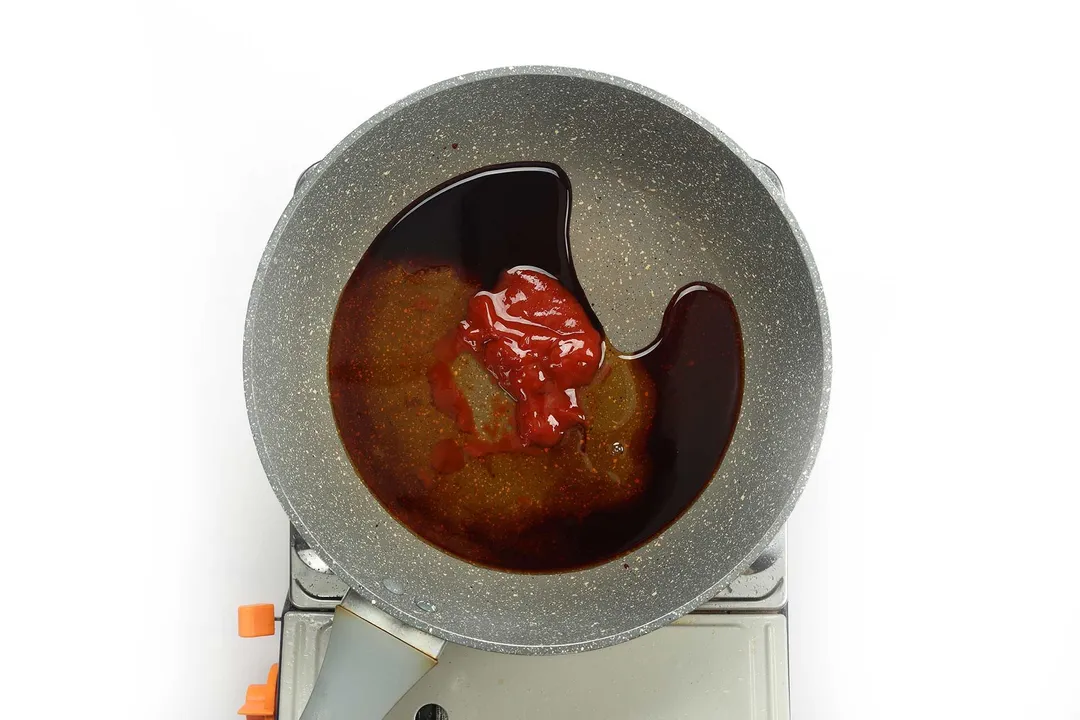 A pan cooking small amounts of soy sauce, honey, and ketchup