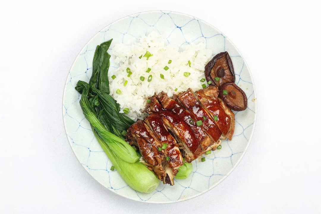 A plate containing a pieces of cooked chicken, mushrooms, white rice, and bok choy