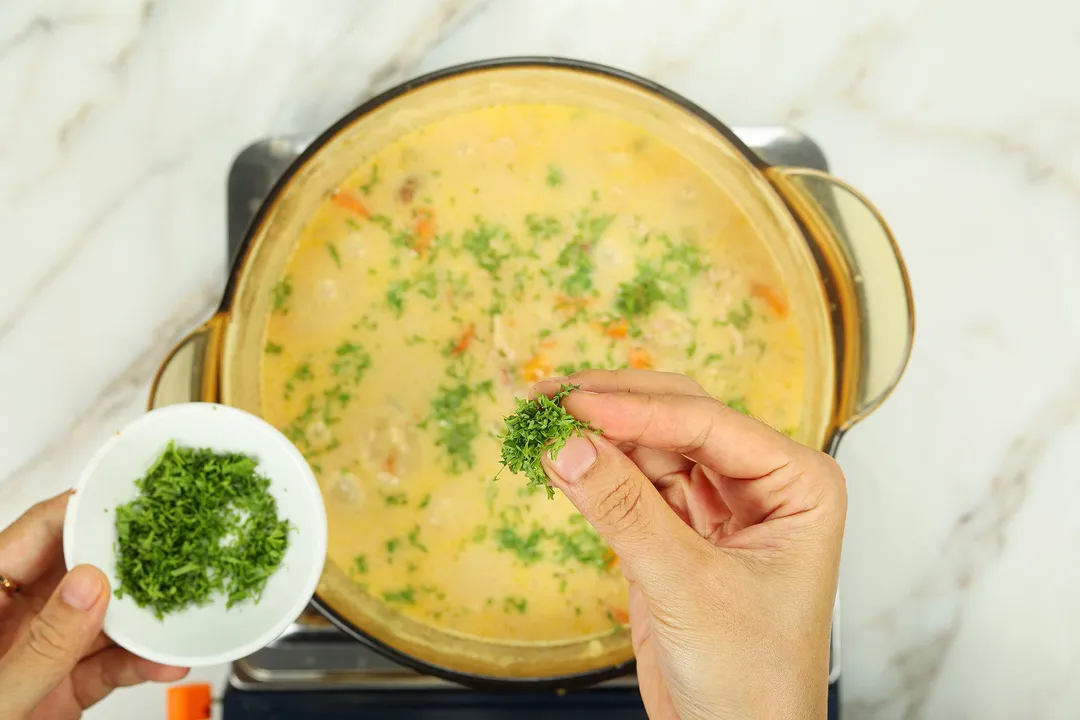sprinkle chopped parsley from a bowl onto a pot of soup