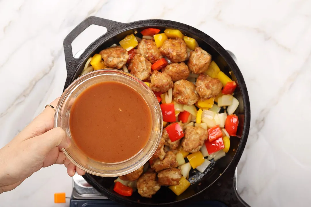 hand holds a bowl of sauce on top of a skillet of chicken manchurian