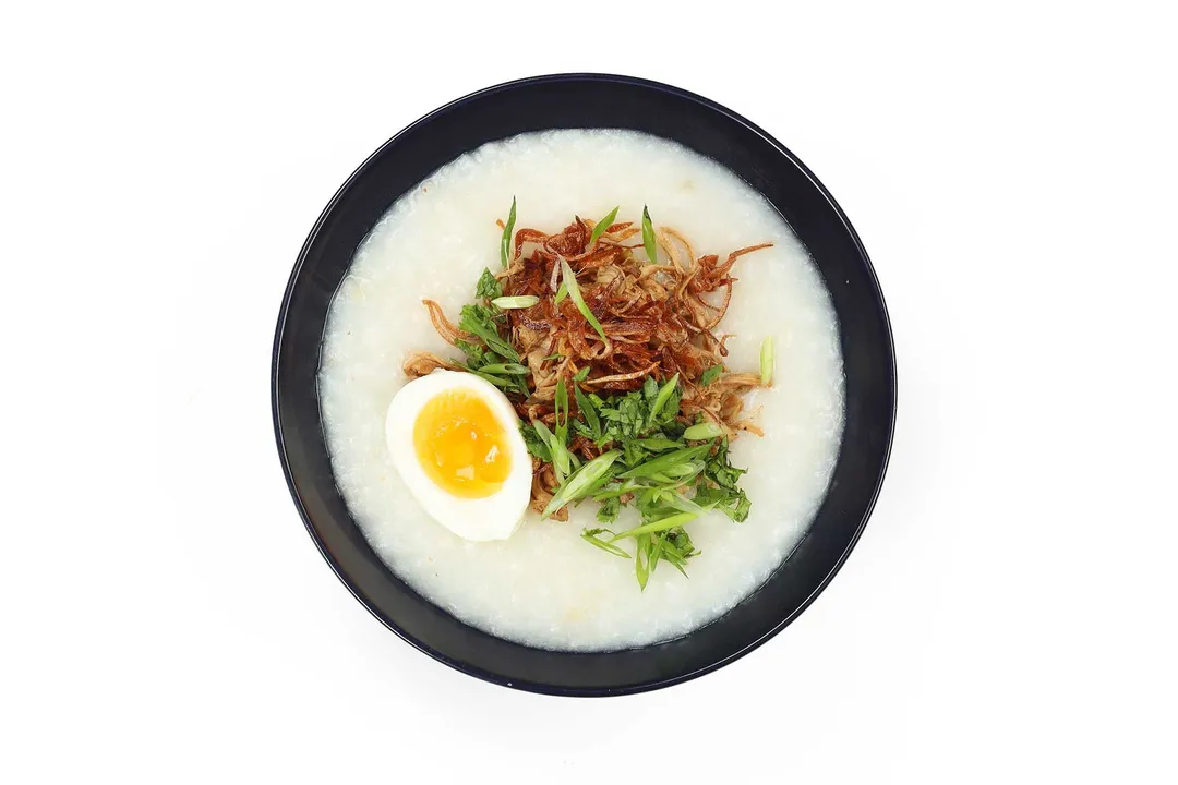 A bowl of chicken congee topped with soft-boiled egg, fried shallots, and herbs
