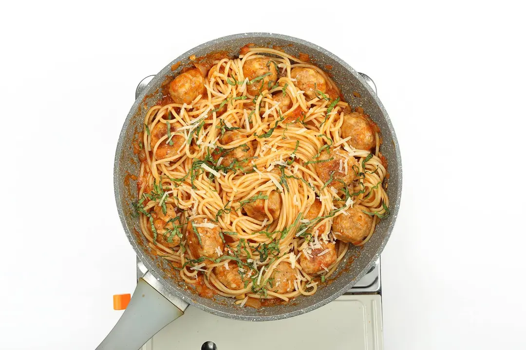 Chicken meatballs served with spaghetti, parsley, and cheese in a pan