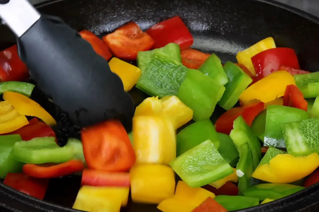 Tongs used to stir fry diced bell peppers