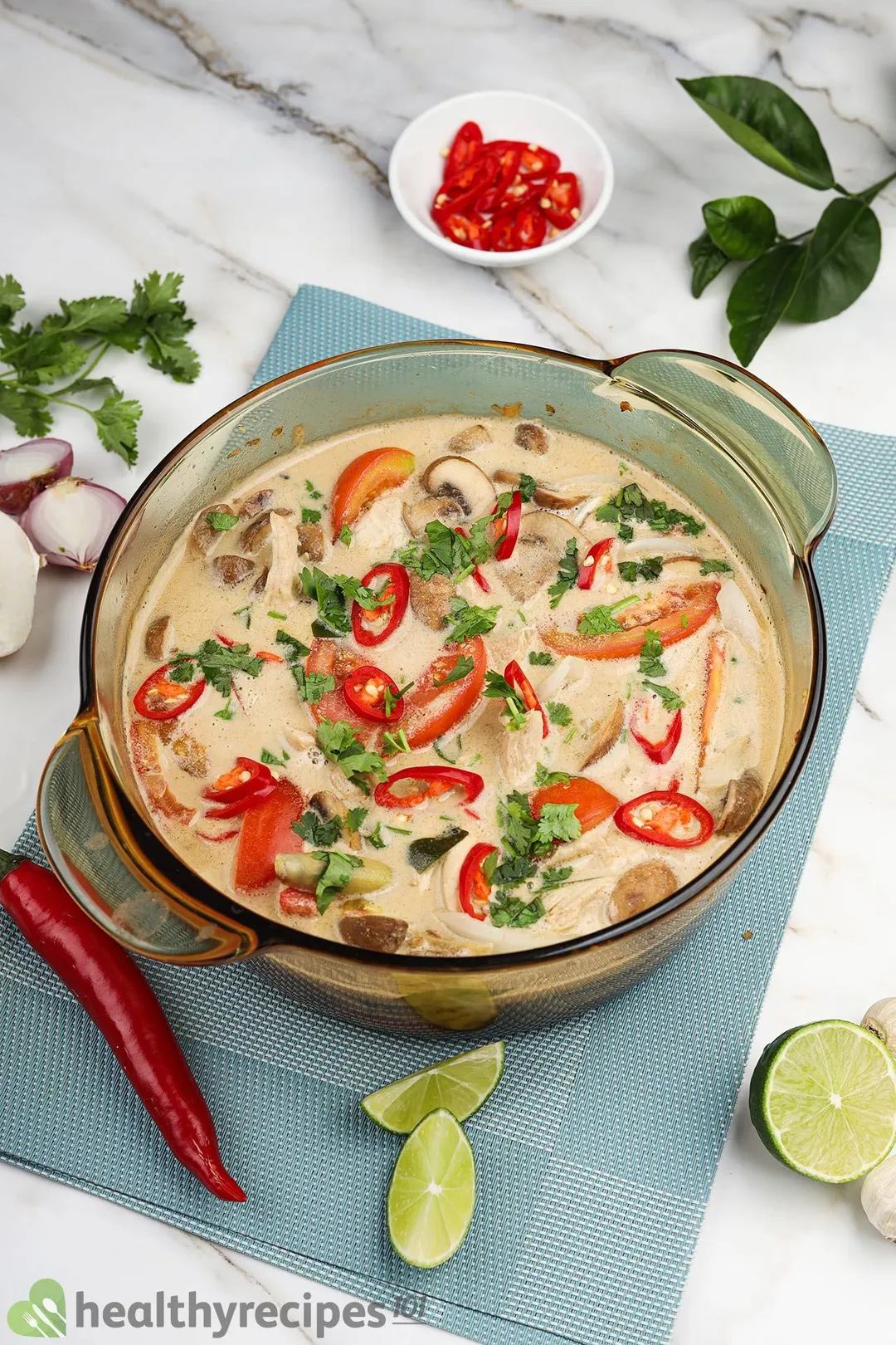 a pot of tom kha soup decorated with a bowl of slices jalapeno, a jalapeno, lime slices