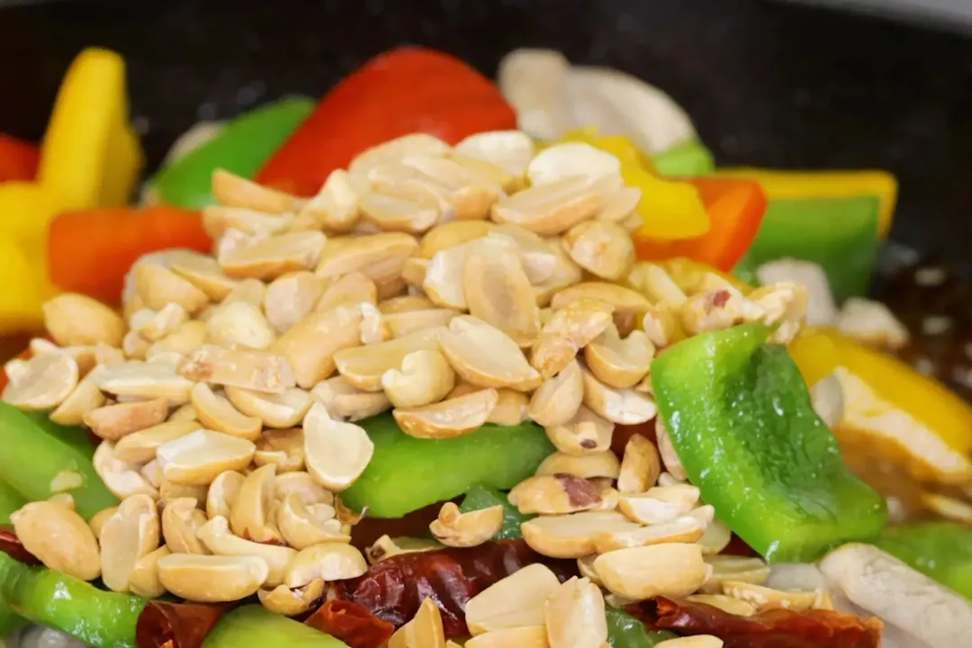 A pile of toasted peanuts laid on a pile of diced bell peppers.