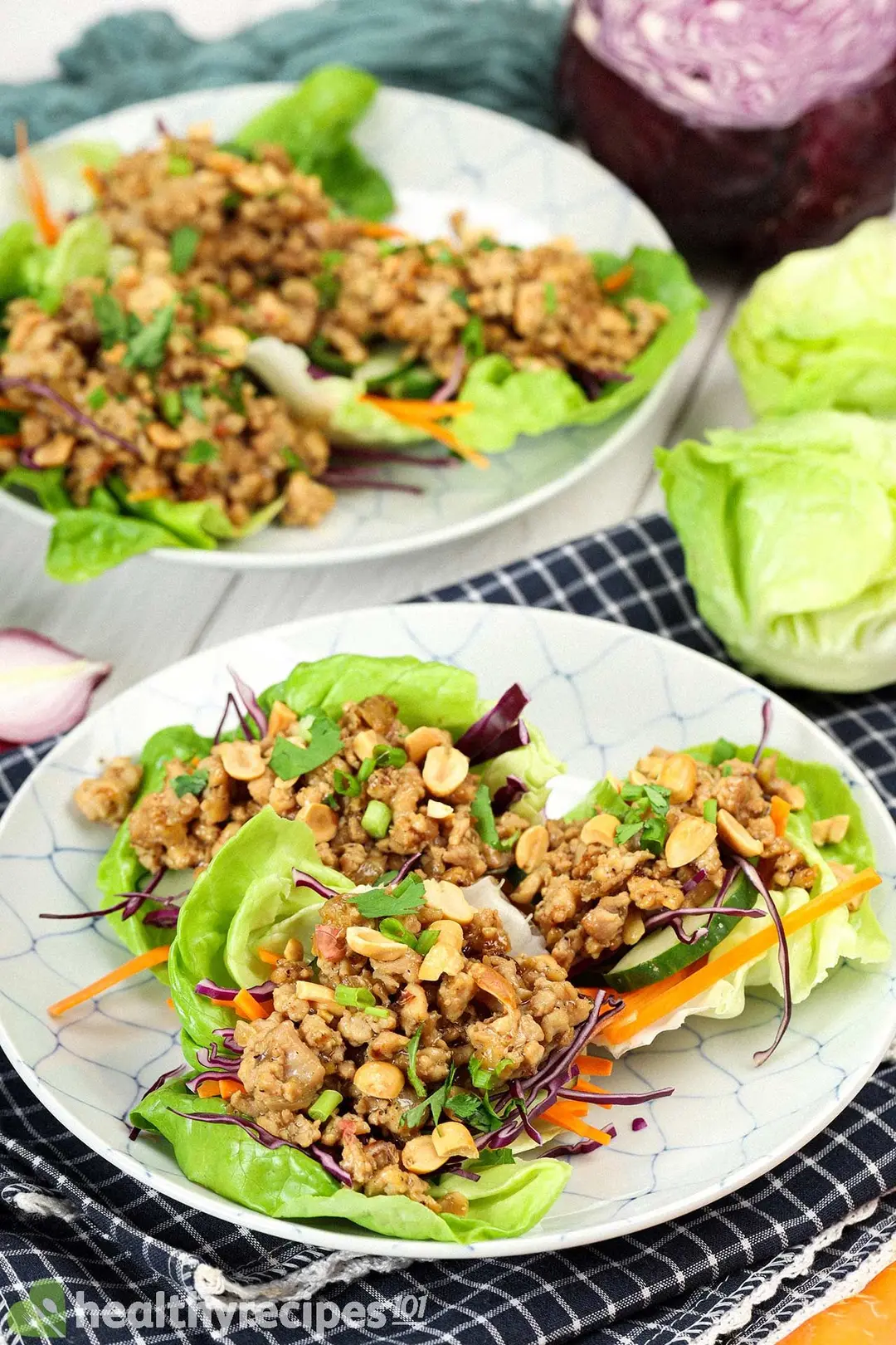 Plates holding lettuce wraps placed on a folded tablecloth and surrounded by lettuce heads and half a red cabbage