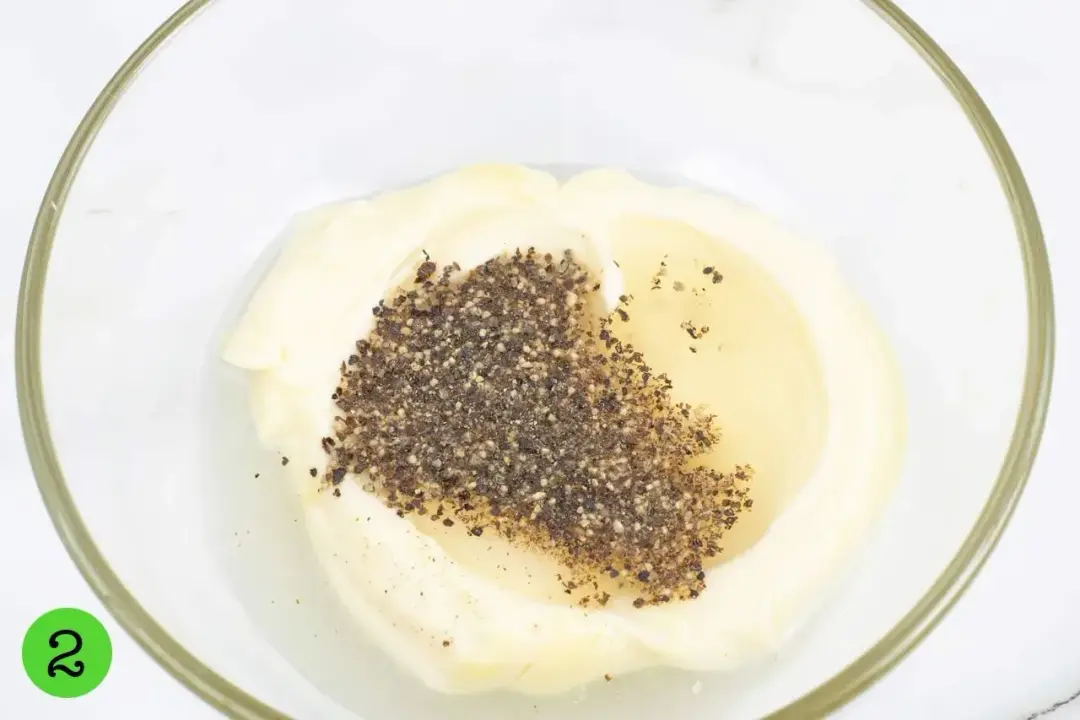 A mayonnaise dressing mixed with oil and ground black pepper in a clear bowl