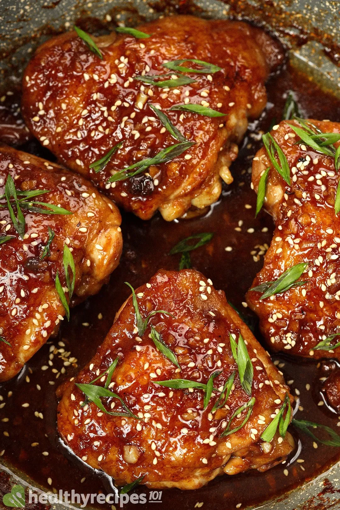 Pieces of cooked and browned chicken thighs covered in white sesame seeds and chopped scallions with a thick and glossy dark brown miso sauce underneath