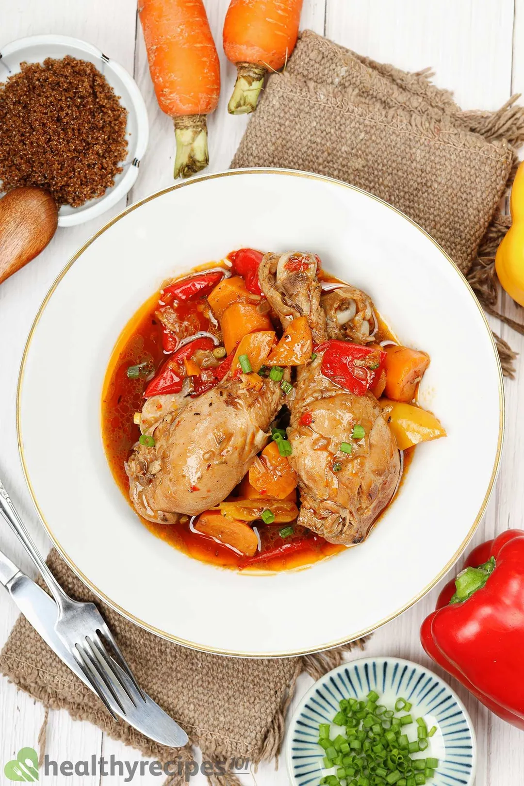 A plate containing a brown sauce, chicken drumsticks, carrot slices, scallions, and bell pepper pieces.