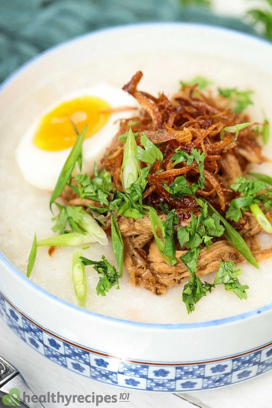 A bowl of chicken congee served with eggs, fried shallots, and herbs