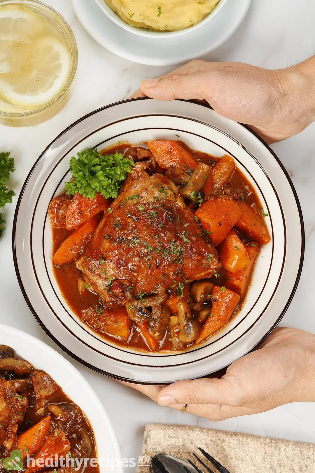 two hands hold a plate of cooked chicken thighs with carrot