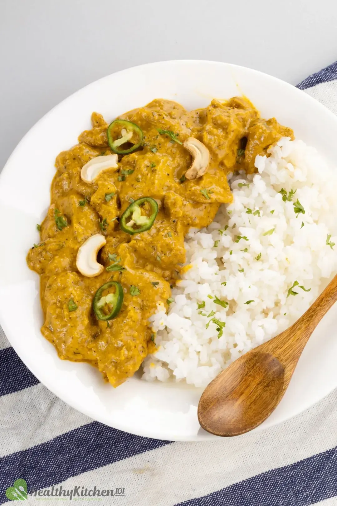 A dish of cooked rice and chicken korma, topped with halved cashews and sliced jalapeños