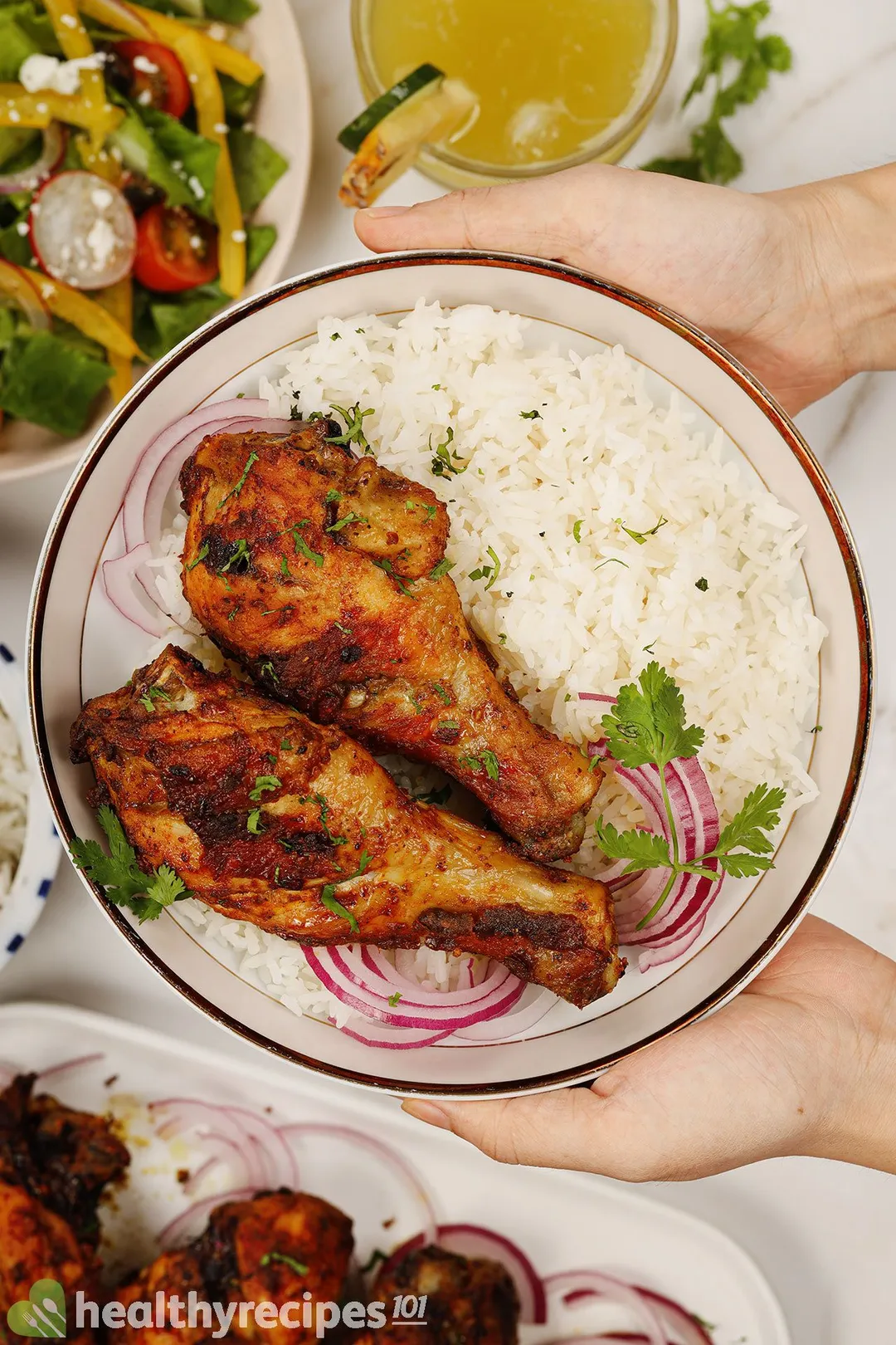 two hand holds a plate of cooked chicken drumsticks and rice