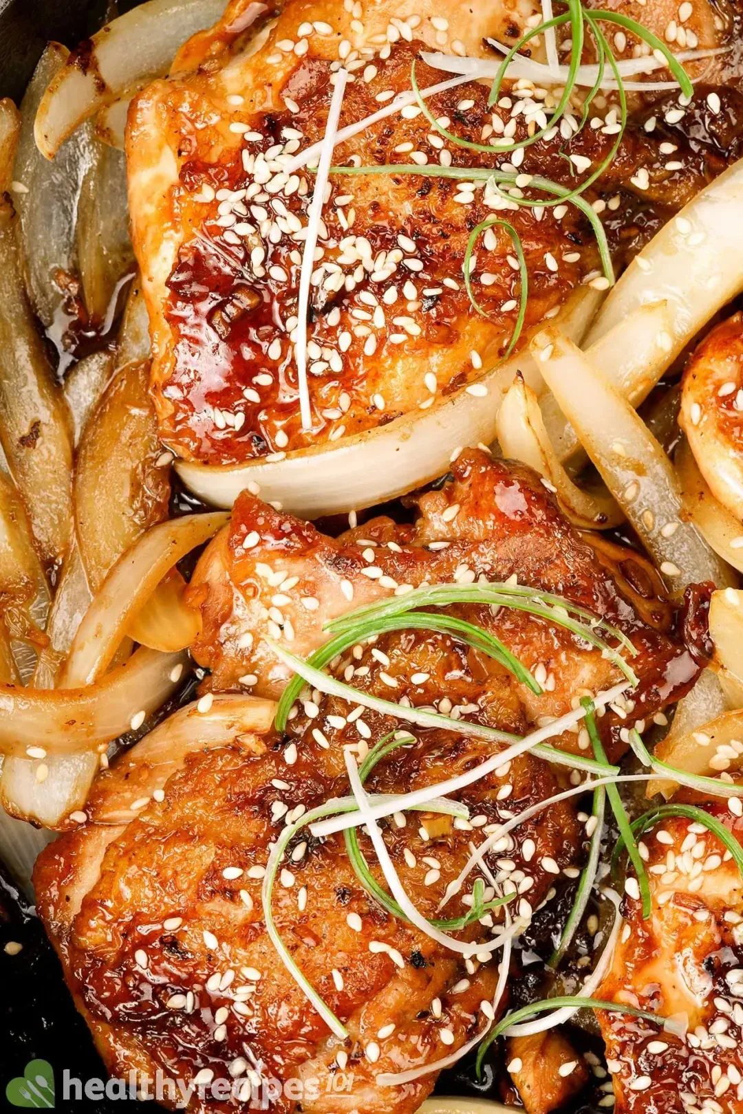 Glossy pieces of teriyaki chicken with sesame seeds, slices of onions, and green onion shaves