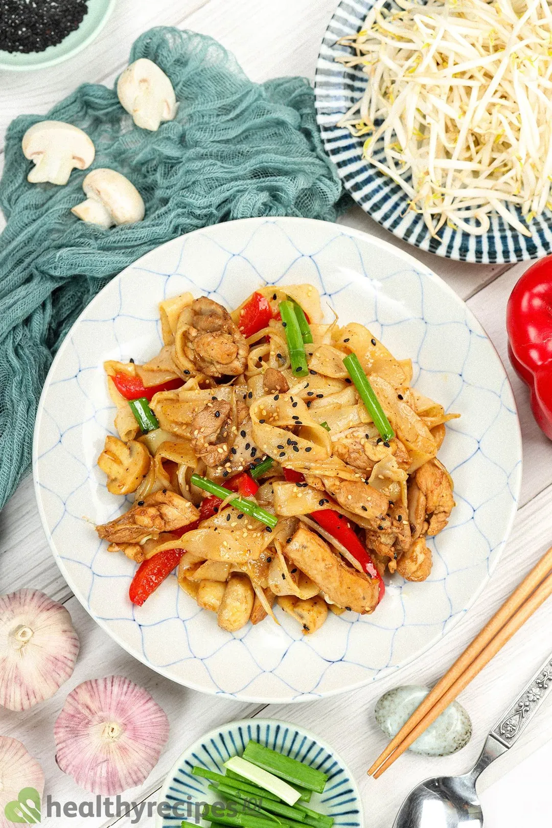 A plate of chicken chow fun decorated with a blue cloth and utensils