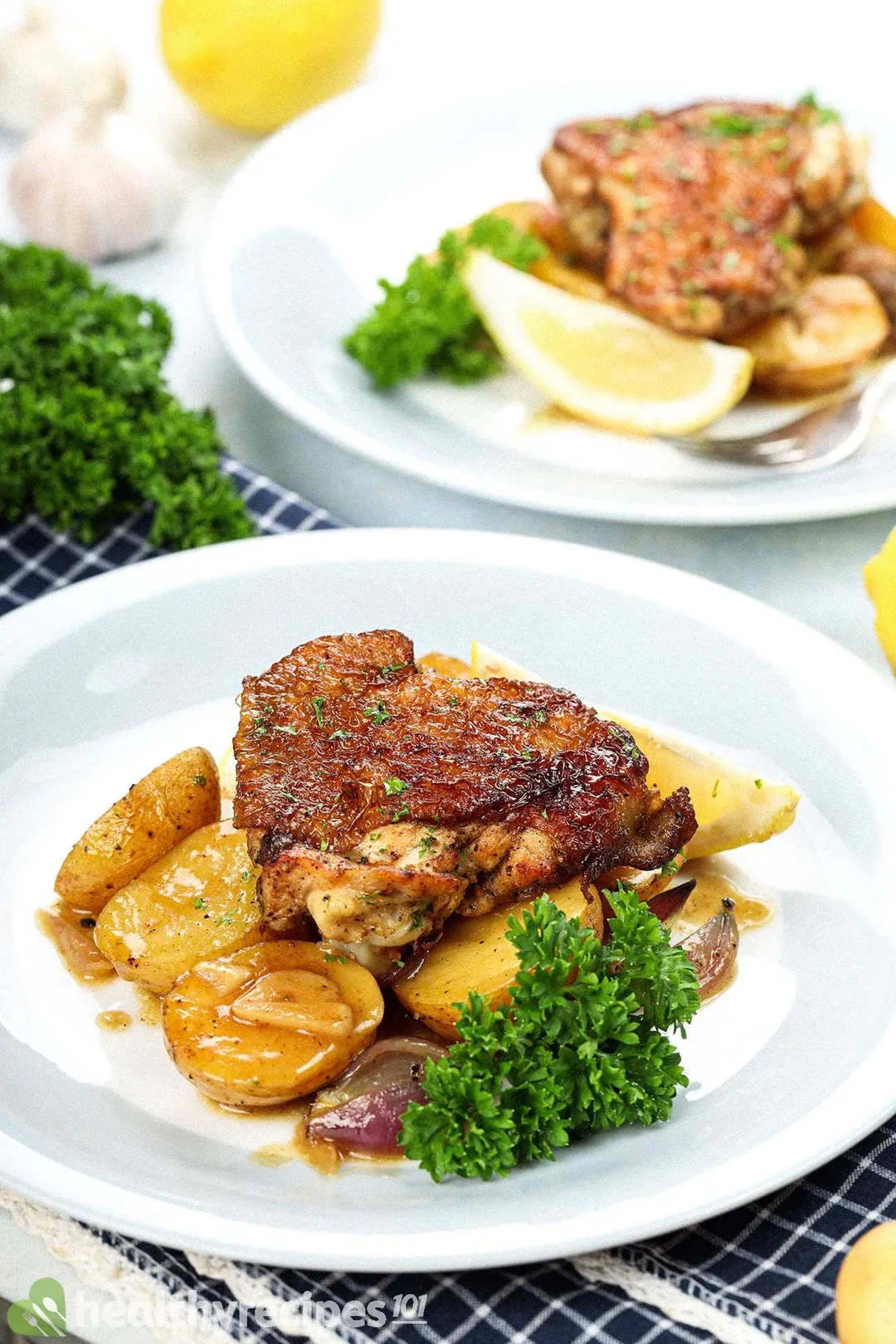 Two plates with browned chicken thighs, halved baby potatoes, and fresh parsley