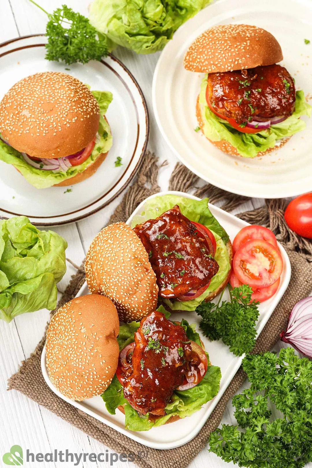 A top-down view of four Buffalo chicken sandwiches on white plates decorated with lettuce, tomatoes, and parsley