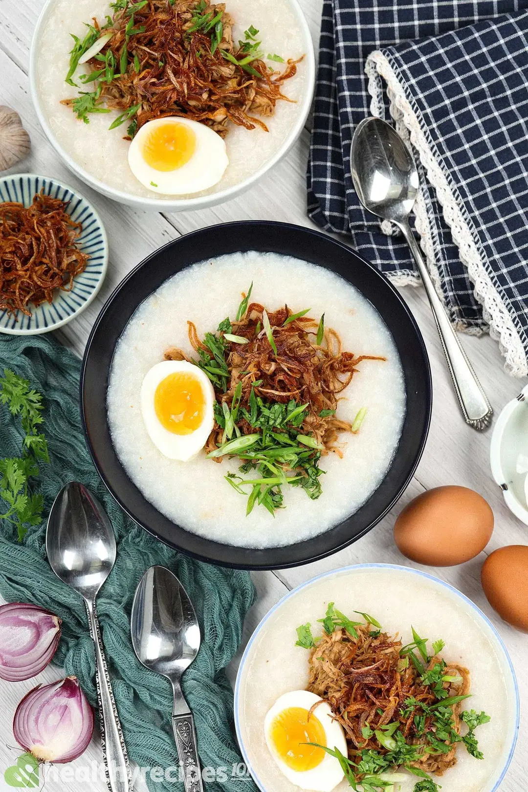 Three bowls of chicken congee alongside fried shallots and utensils