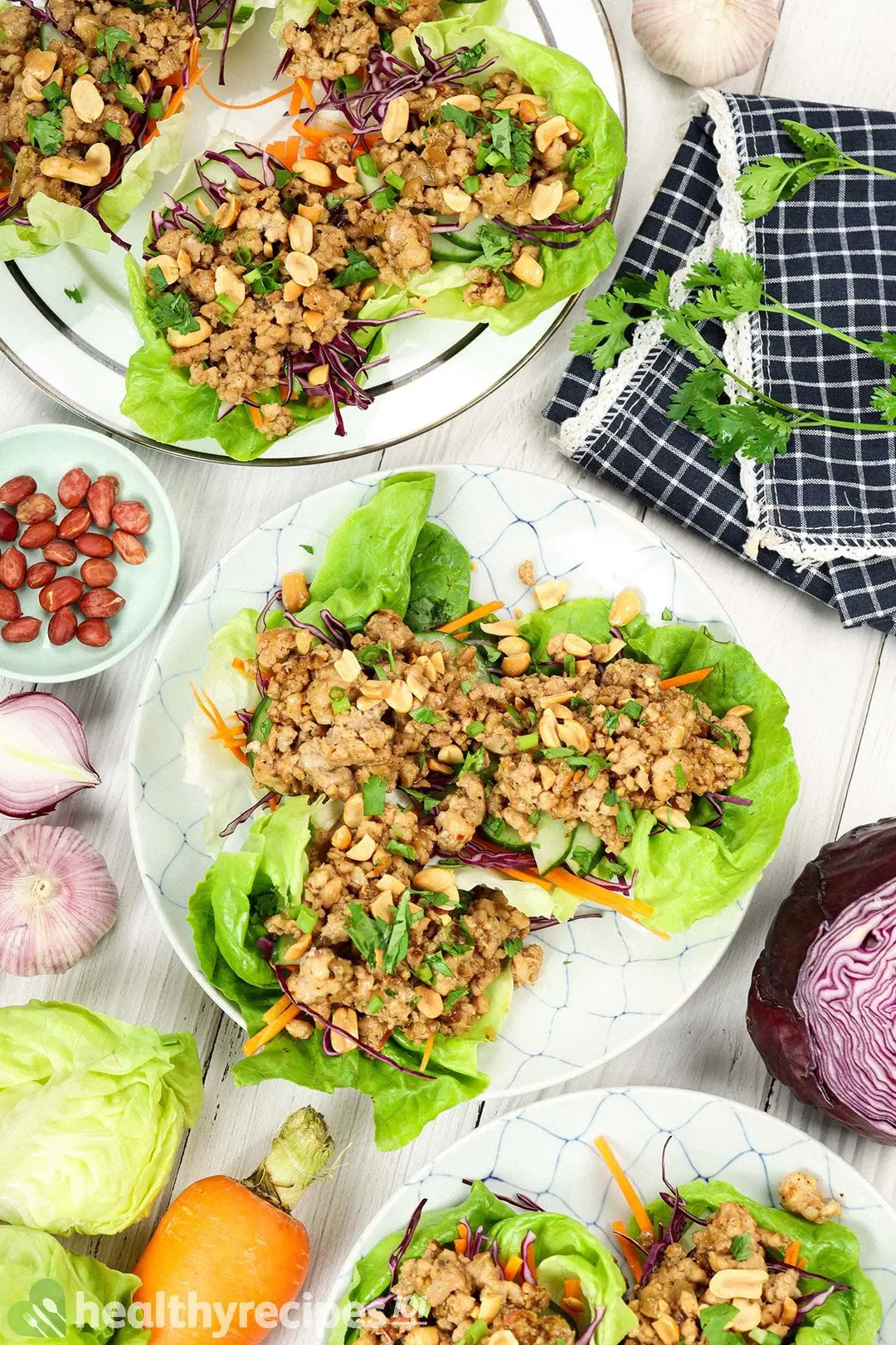 A flatlay of lettuce wrap dishes, cabbage heads, carrots, red onions, peanuts, coriander, and half a red cabbage