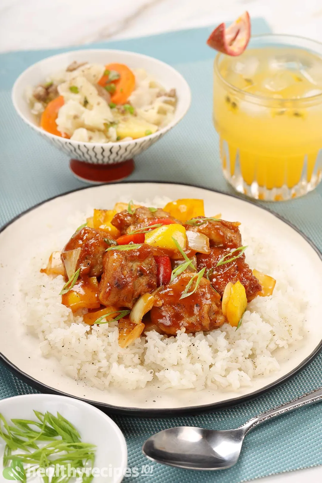 a plate of cooked chicken manchurian with rice next to a glass of juice and a bowl of cabbage soup