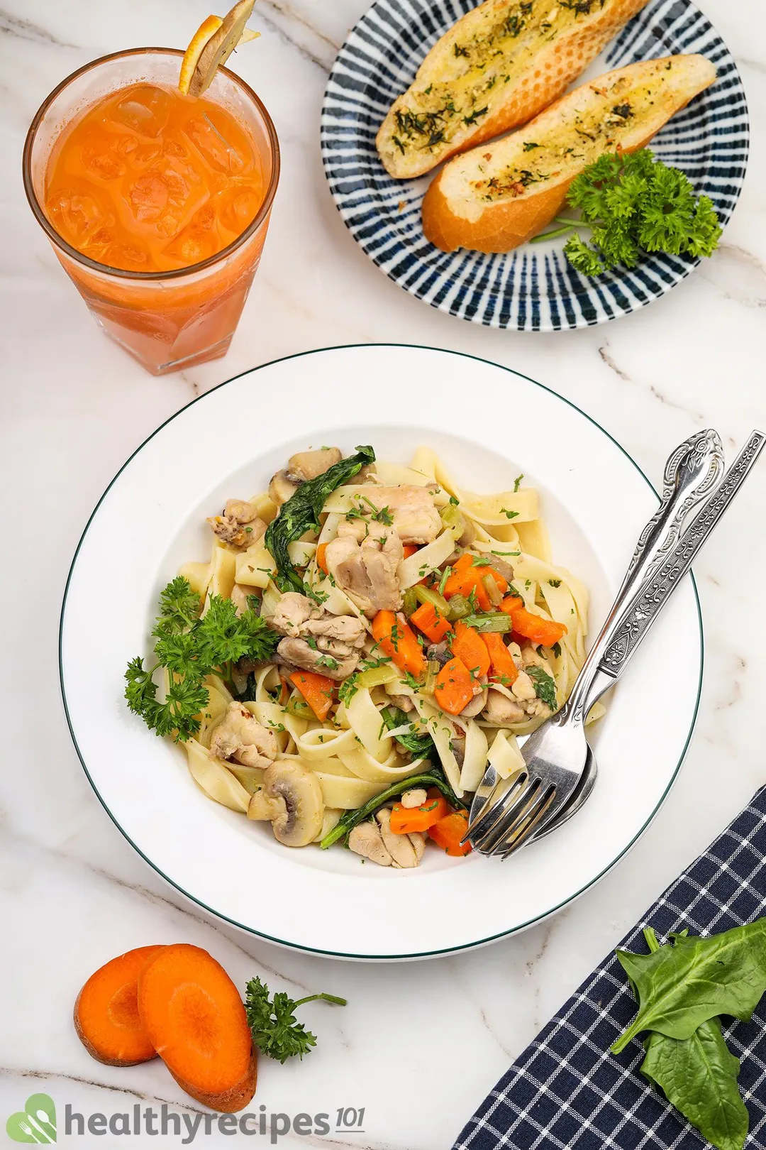 a plate of chicken noodle soup next to a glass of carrot juice, two bread slices on a plate