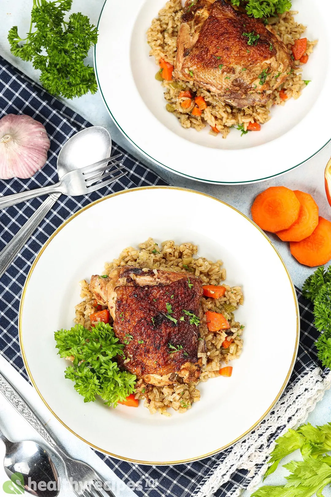 Two plates of chicken rice decorated with utensils and a blue tablecloth