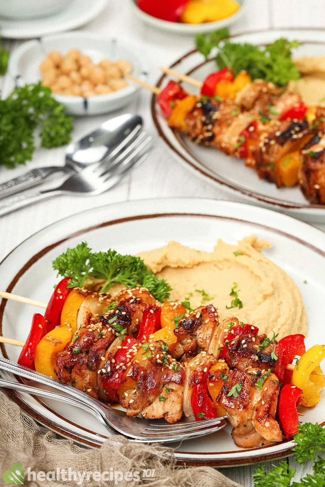 Two plates of chicken skewers with chickpea puree decorated with utensils