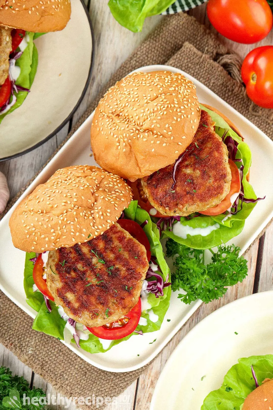 A high-angle shot of two hamburgers placed on a rectangle plate and decorated with parsley leaves