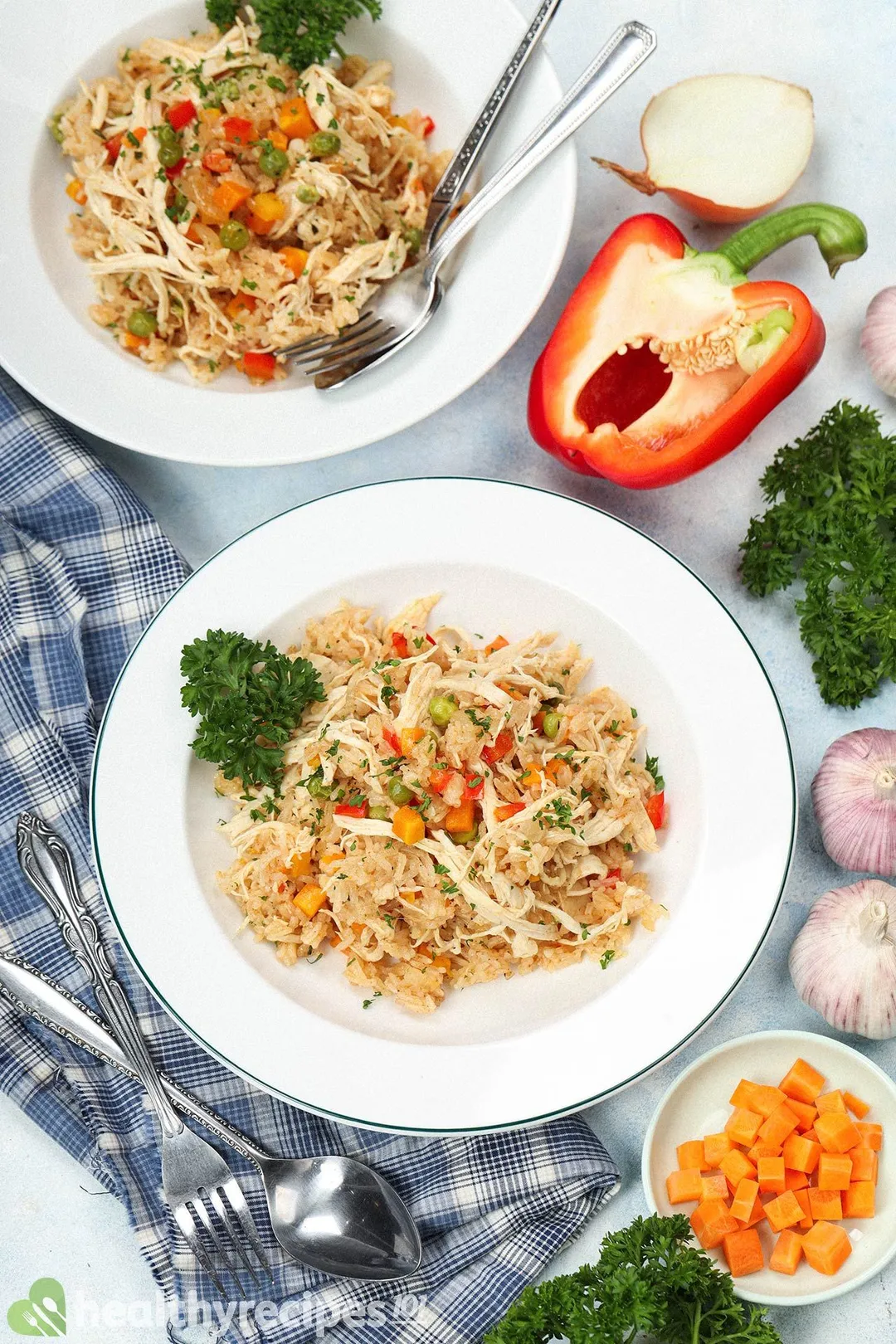 A flatlay of rice dishes, a blue tablecloth, some diced carrots, half a bell pepper, and half an onion