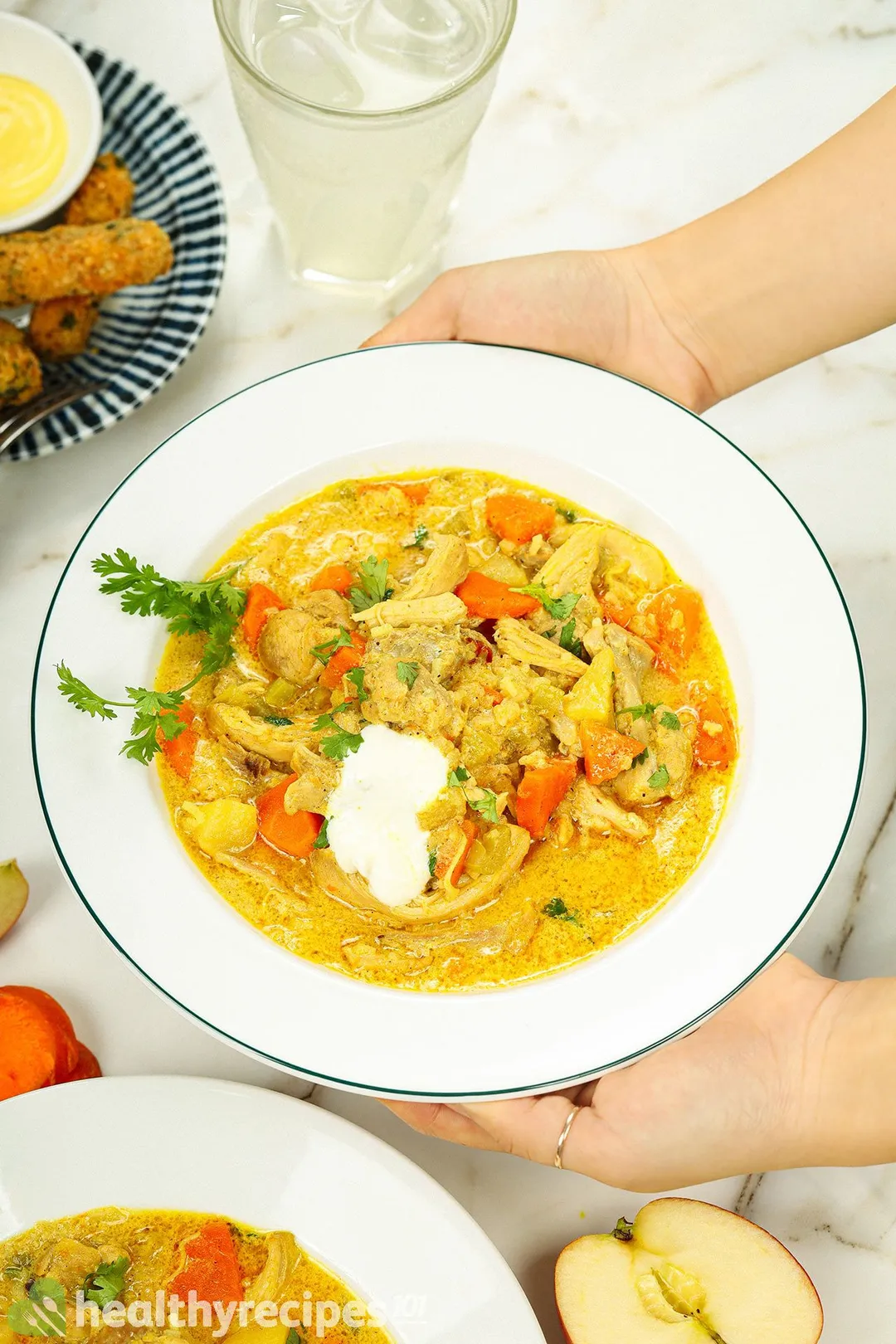 two hand holds a plate of mulligatawny soup next to a glass of juice and a plate of zucchini fries