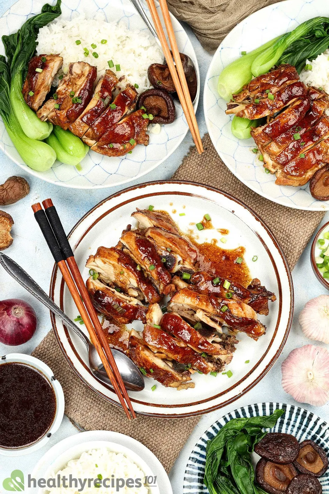 A plate of cooked chicken sliced crosswise into medium pieces, placed next to spoons, chopsticks, and other plates containing various foods