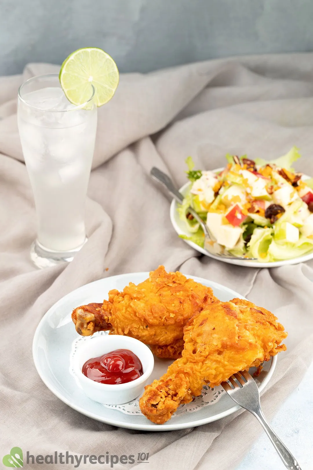 a plate of two cooked chicken drumsticks next to a plate of salad and a glass of juice