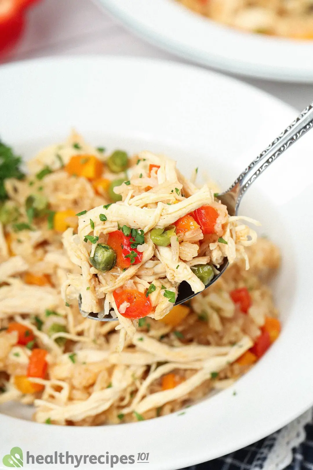 A spoon holding some rice, shredded chicken, diced bell peppers, and green peas