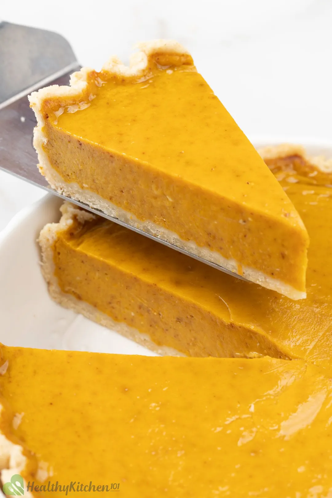 A piece of pumpkin pie being lifted from the whole pie.
