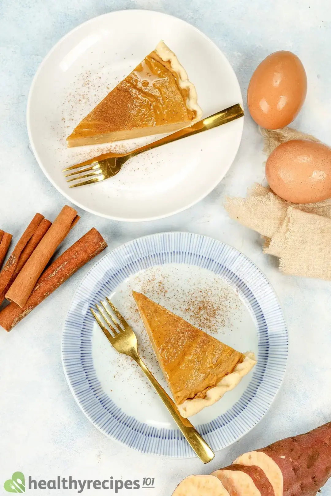 two pieces of Sweet Potato Pie on two plates with forks decorated by two eggs sliced sweet potatoes and cinnamon sticks