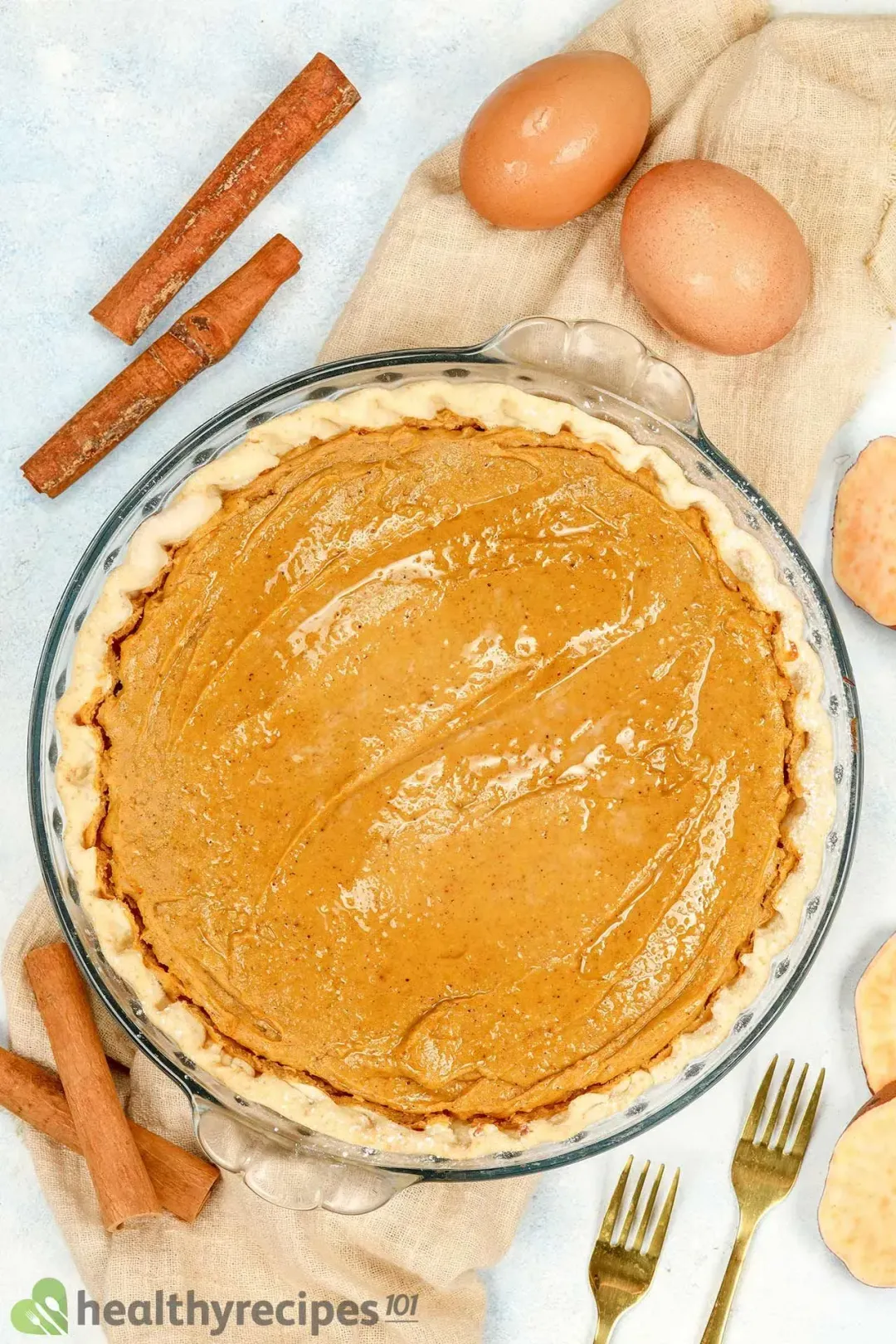 a sweet potato pie surrounded by two eggs, fork and cinnamon