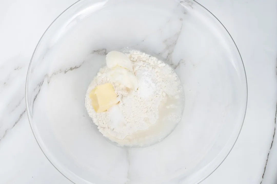 A large glass bowl with some flour and butter in the center
