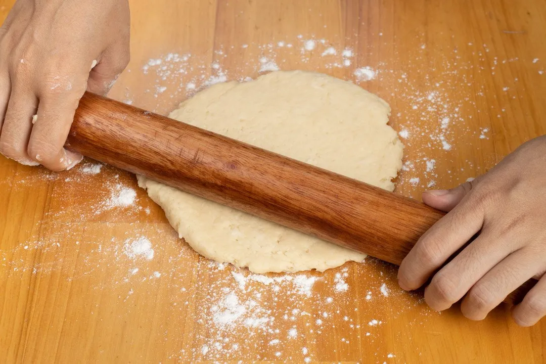Two hands using a roller to flatten a pie dough.