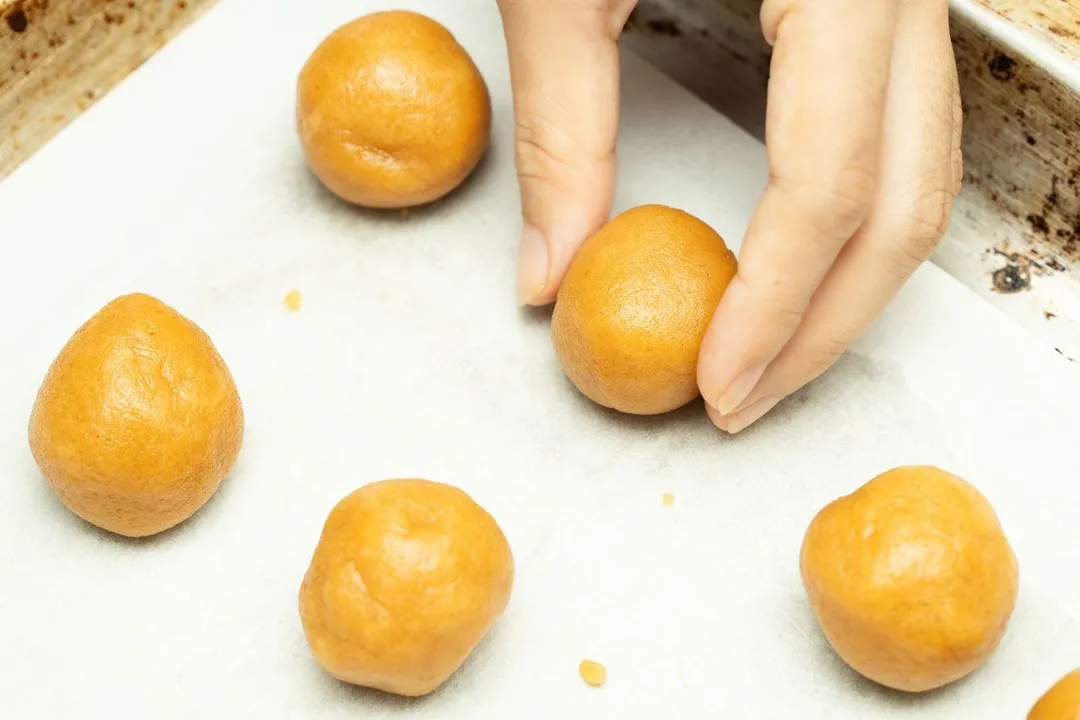 hand holds a ball on a baking tray with other balls