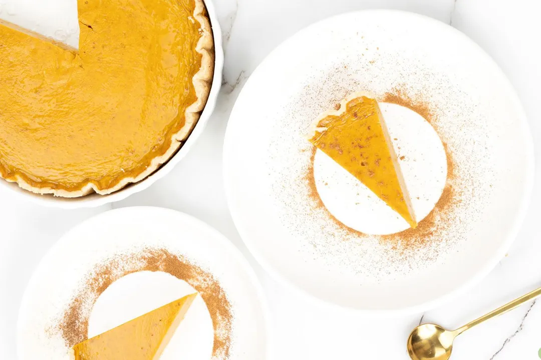 A high angle shot of a spoon, pumpkin pie slices and a pumpkin pie.